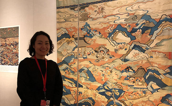 Textile conservator Minsun Hwang posing in front of "Panel with boys at play" tapestry
