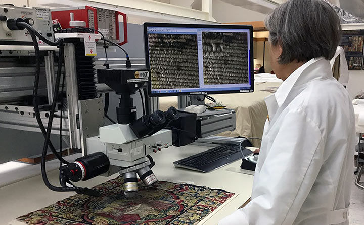 Conservation scientist in a white lab coat looking at a textile under a microscope in the lab
