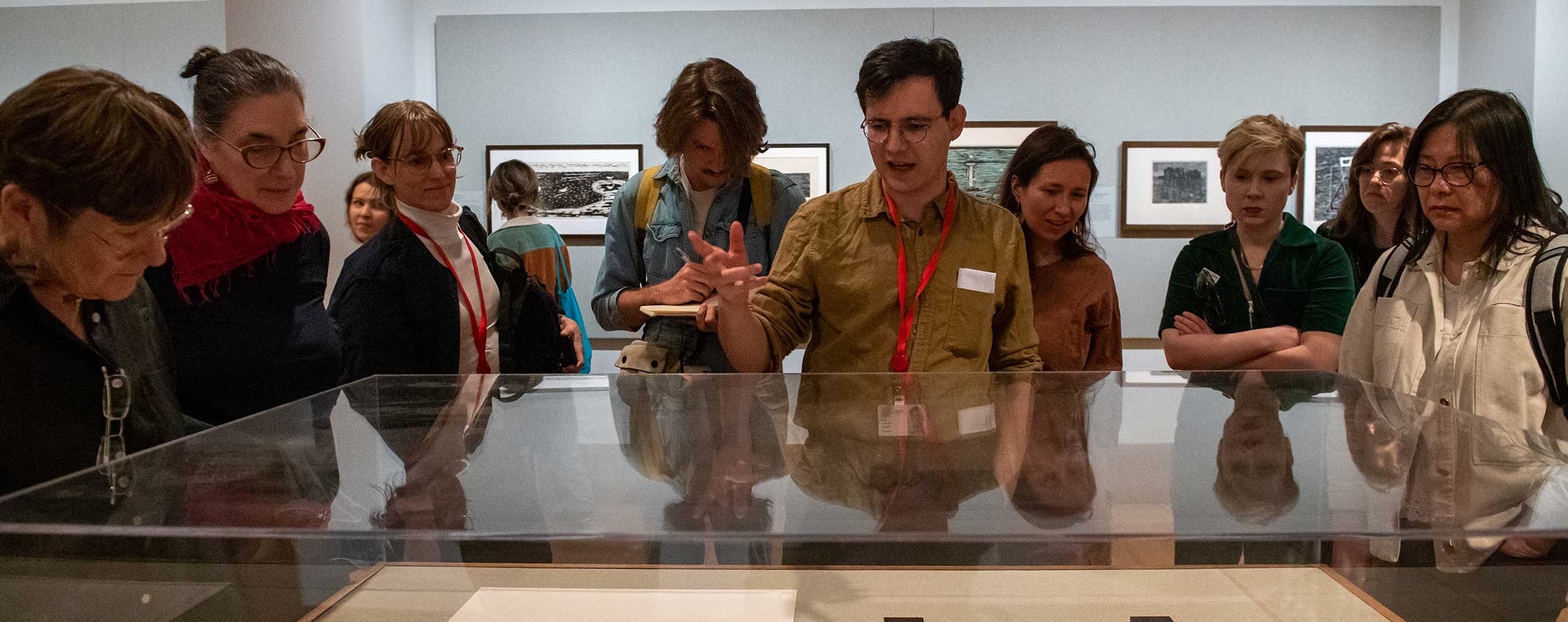 Fellows observe antiquated documents in a protective a glass cabinet in a museum gallery.