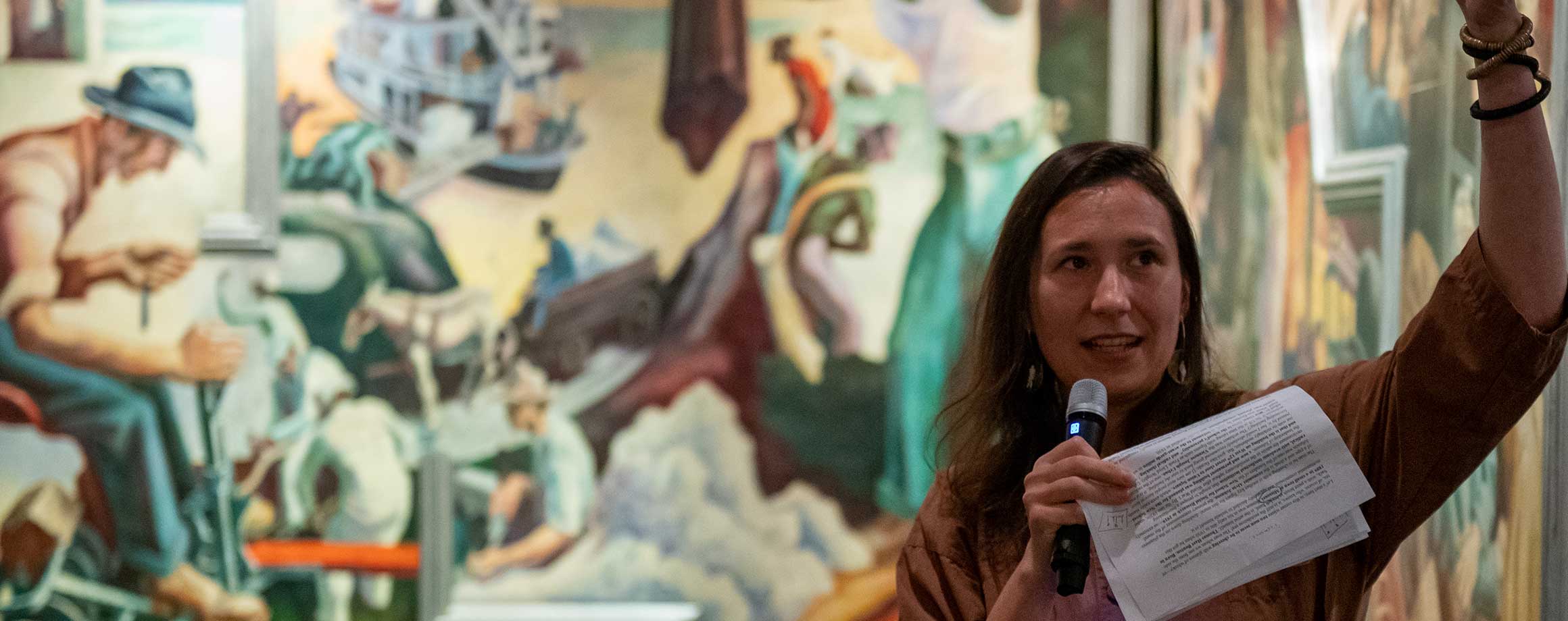 A fellow holds a mic and gives a presentation in a gallery