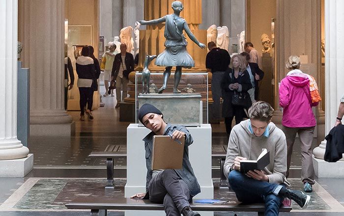 Two young men sit on a bench drawing in the Greek and Roman gallery