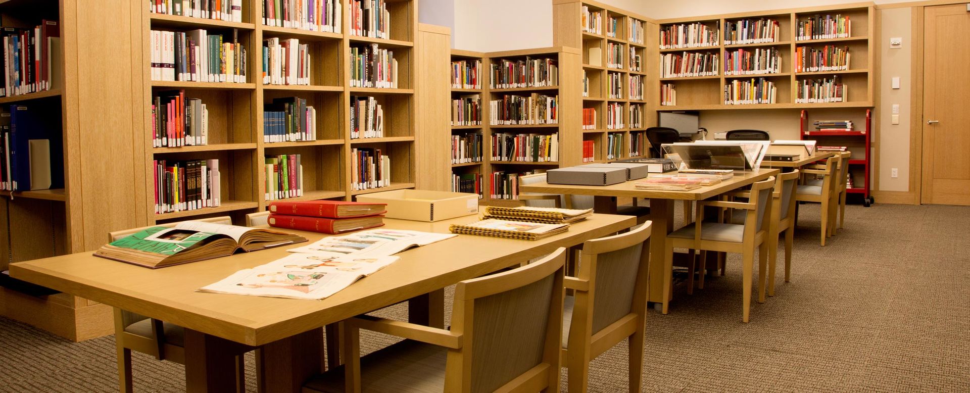 A bright, modern, blonde wood library lined with shelves of books and tables with comfortable chairs