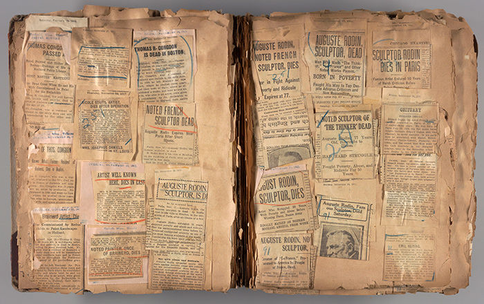 An open scrapbook filled with overlapping, yellowing newspaper clippings, many about the death of Auguste Rodin