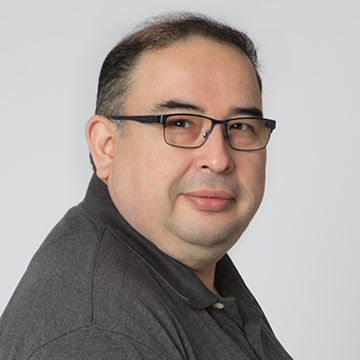 A man with graying dark hair and glasses, wearing a dark gray, open-collared shirt