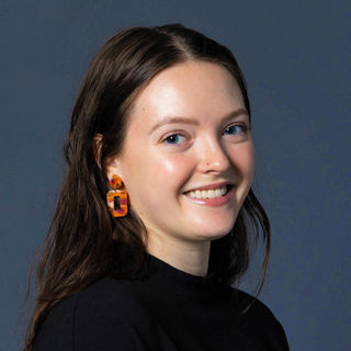 A smiling woman with brown hair, wearing orange earings and a black shirt