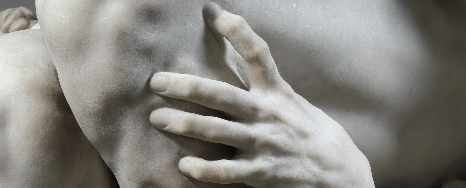 Detail view of a marble sculpture in which we see a hand grasping another piece of flesh