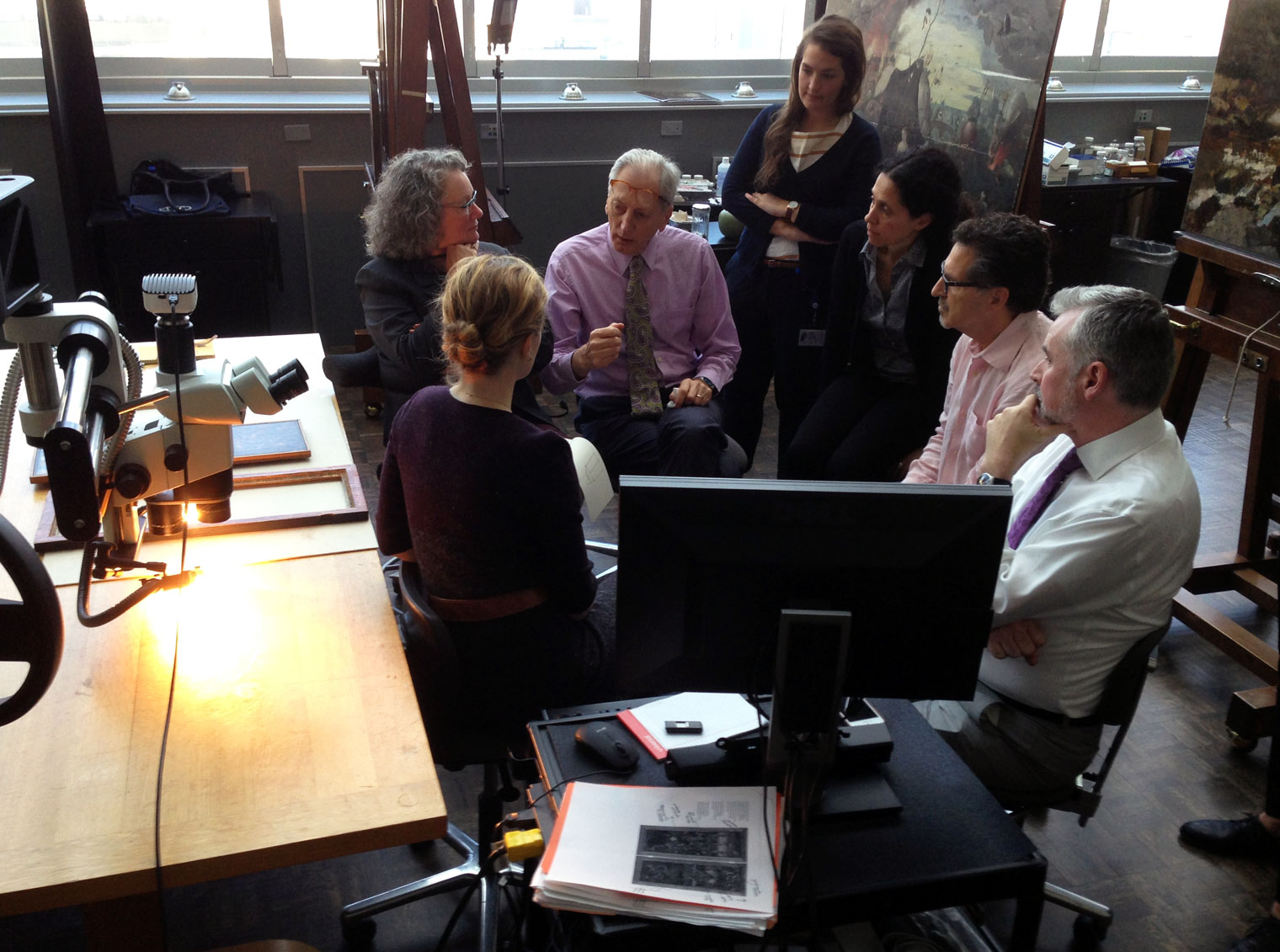 A group of art experts hold a discussion in a brightly lit conservation studio