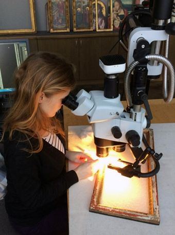 A conservator examines a wood frame using a microscope