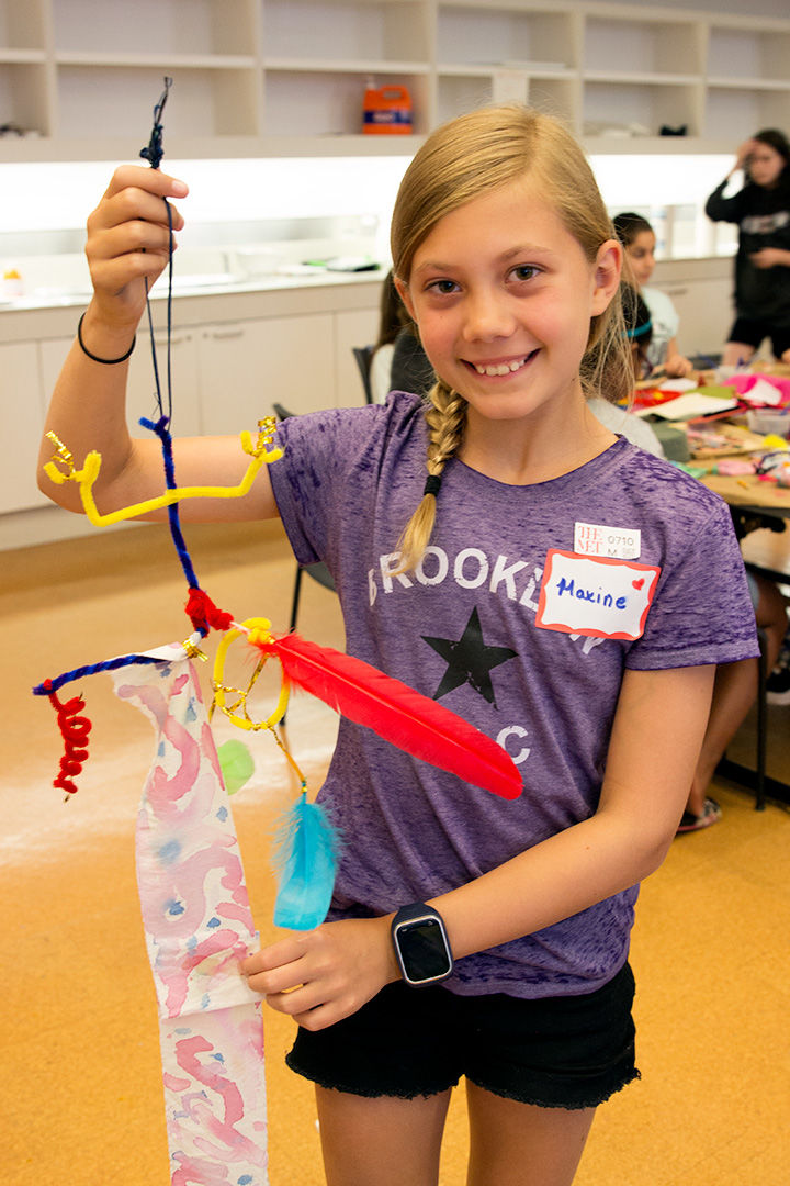 Max holds up her finished mobile made of dyed cloth, pipe cleaners, string, and other materials.