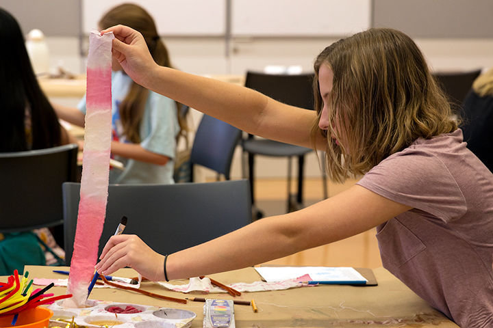 A teen dips a strip of cloth into pink dye.