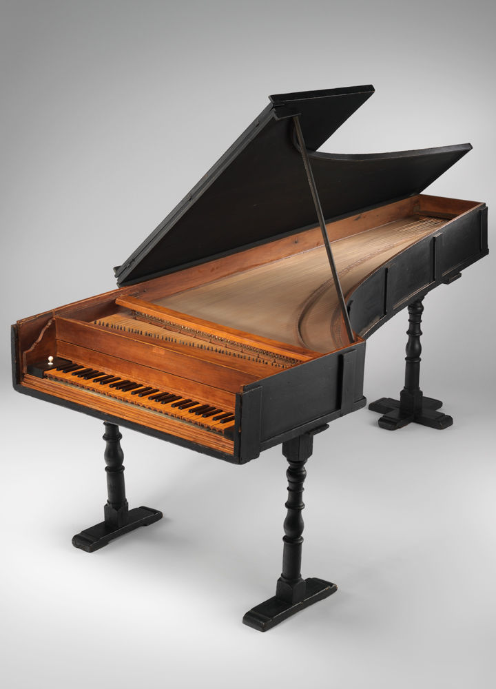 Picture of one of the world's oldest pianos, made by Bartolomeo Cristofori. The outside of the piano is black. The lid is propped up, revealing the honey-brown inside of the instrument.