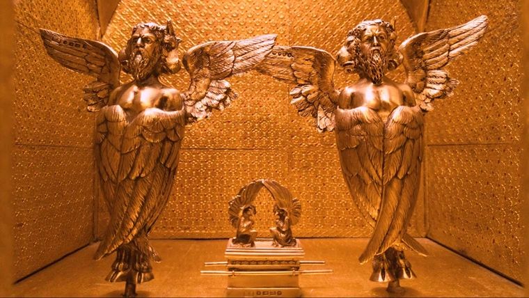 A golden model room with two gold statues of ancient angels and an ornate cabinet between them.