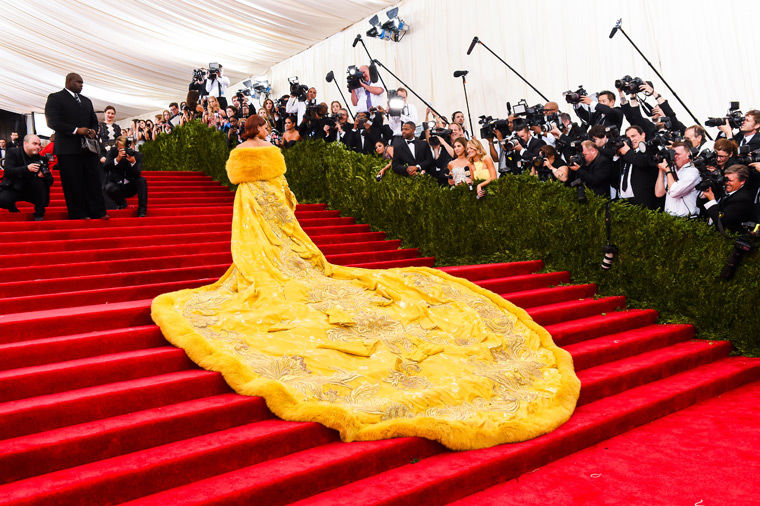 Rihanna walks up the main stairs of the red carpet at the 2015 Met Gala wearing an elegant, yellow couture gown by Guo Pei