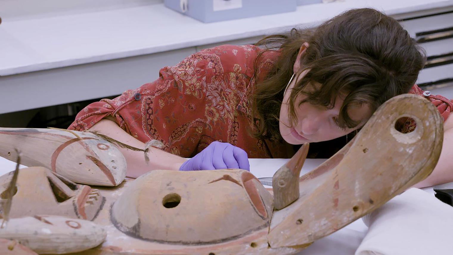 A woman leans over a yupik mask in a scientific lab
