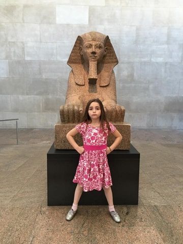 A photograph of a young girl posed in front of a statue in the Egyptian Wing at The Met.