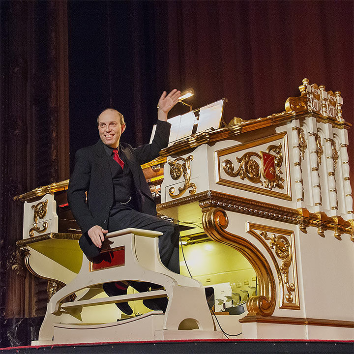 A photograph of the pianist Ben Model waving on the stage of a grand theater