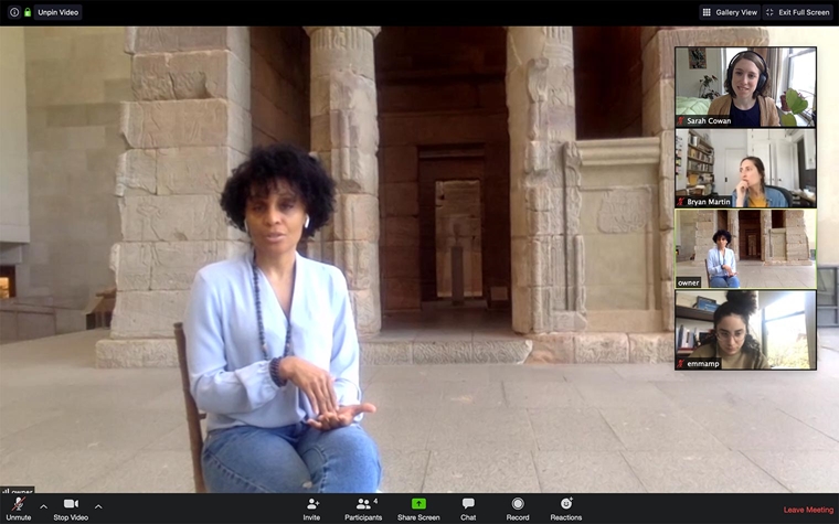 A zoom screen capture of a seated woman in front of an ancient temple at The Met being interviewed by a production crew visible in windows on the right of the screen.