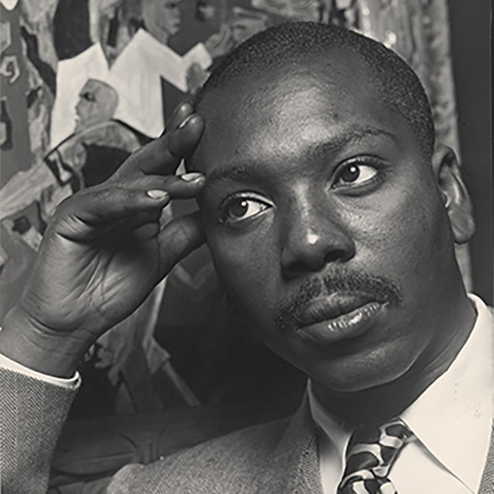 A black-and-white photo of Jacob Lawrence resting his head in his hand in front of one of his paintings