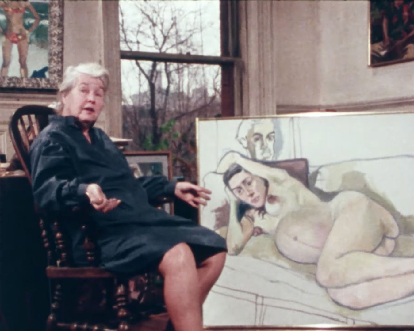 Alice Neel seated in a chair in front of a large painting of a nude pregnant woman