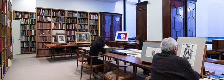 A man looks at a drawing in a room surrounded by books