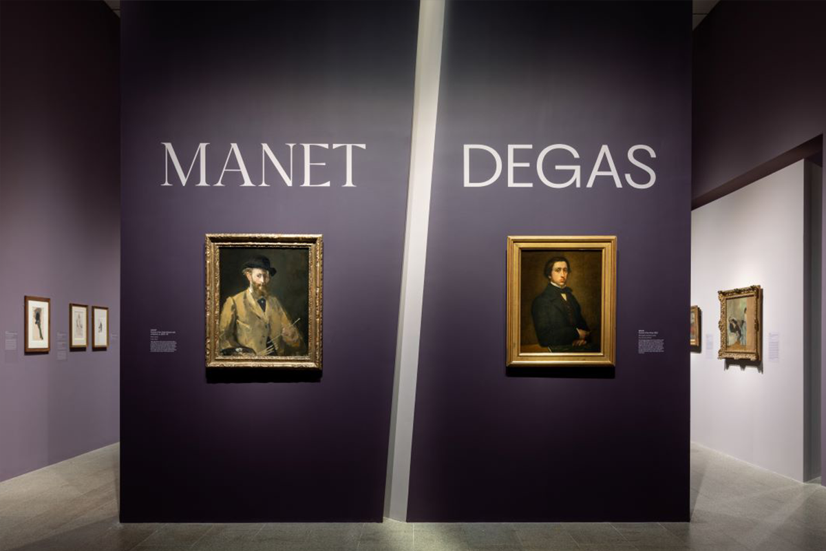 The entry to Manet/Degas. Features a purple wall with white text that reads Manet/Degas above two self-portraits by the respective artists.