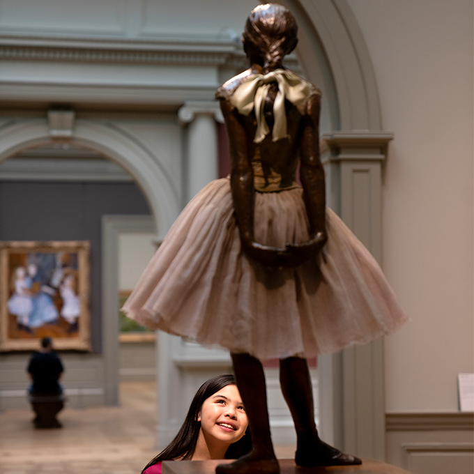 A young girl smiles as she views Degas' "The Little Fourteen Year Old Dancer" a bronze sculpture of a ballerina.
