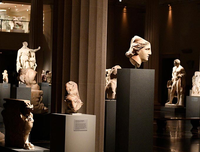 Busts and statues from Ancient Greece rest upon pedestals in a gallery in The Met