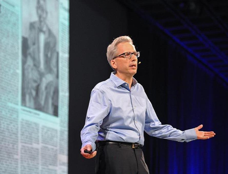Man with headset microphone in front of a large screen, lecturing