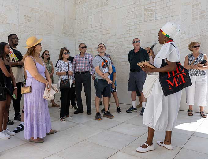 Visitors dressed in summer clothes listen to a gallery talk by a Met expert.