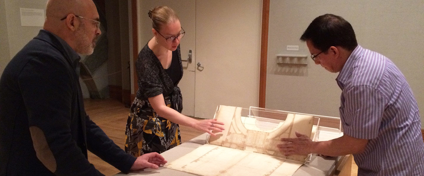 A woman and two men install an architectural model in a gallery