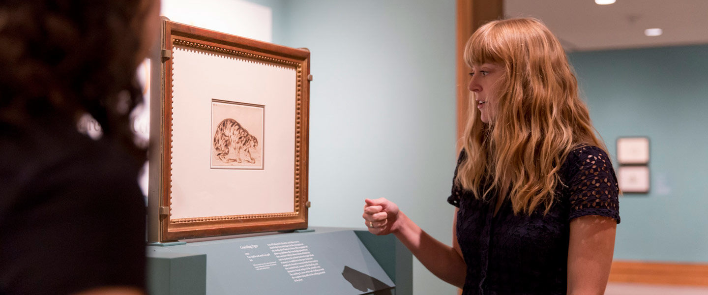 A female curator discusses an artwork in an exhibition gallery with a group tour