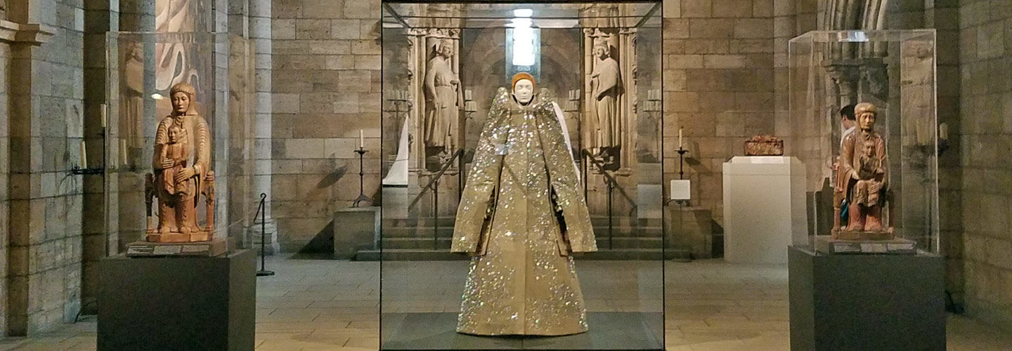 View of a gallery in a medieval cloister, featuring two twelfth-century sculptures of the Virgin and Child on either side of a contemporary ensemble by Viktor & Rolf