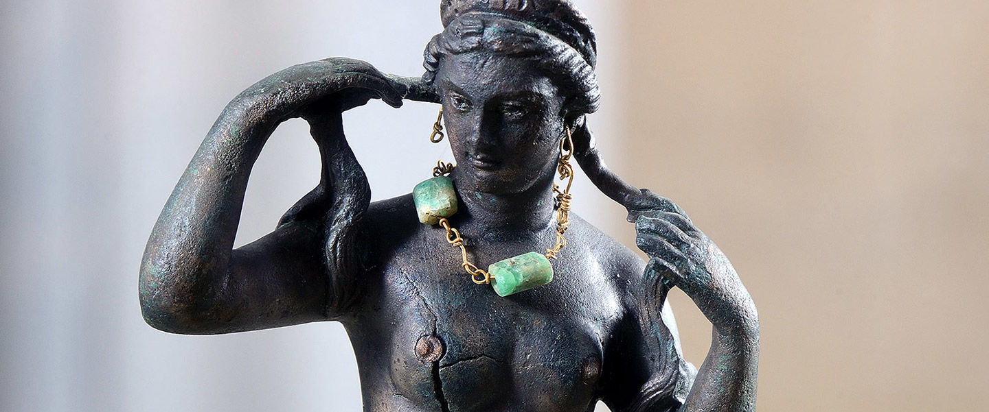 Detail of bronze figurine holding her locks of hair and wearing a necklace with two huge emeralds