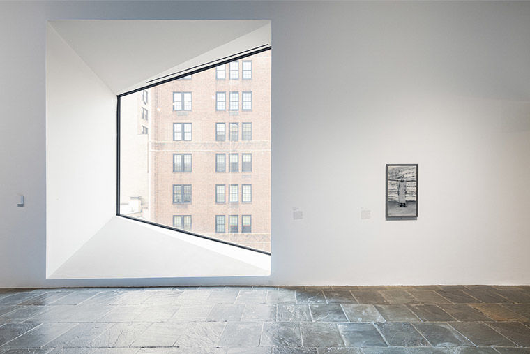 Installation view of Gerhard Richter: Painting After All featuring a small, greyscale painted portrait of a man in uniform next to a large, trapezoidal window