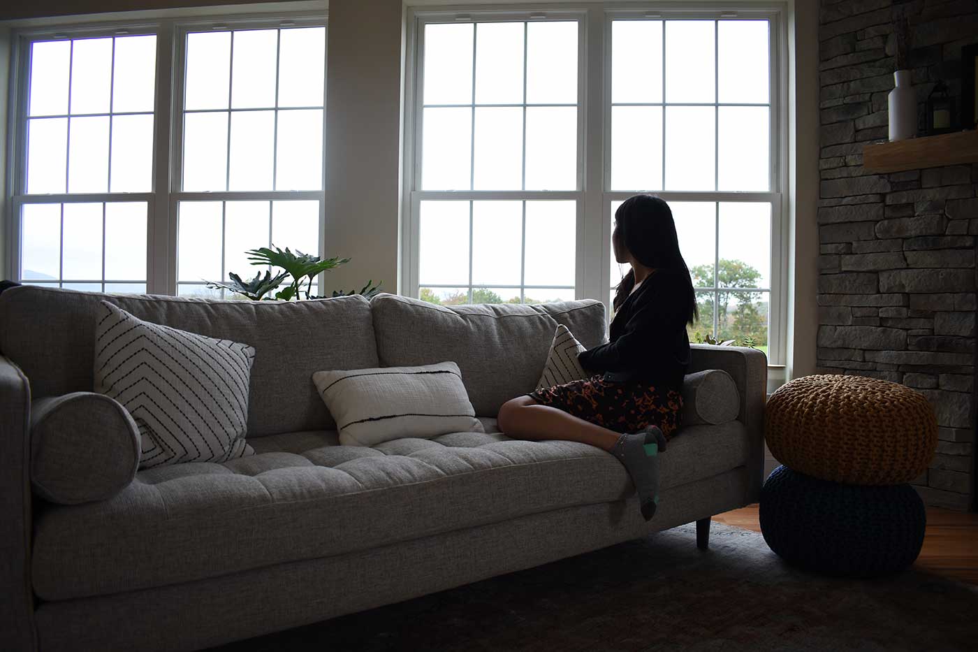 photograph of a person sitting on a couch looking out large windows.