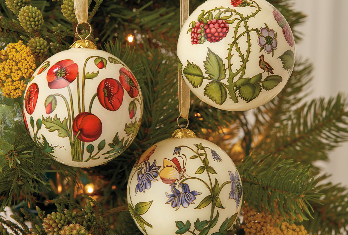 Three white christmas ornaments with floral motifs hang from branches of a pine tree.