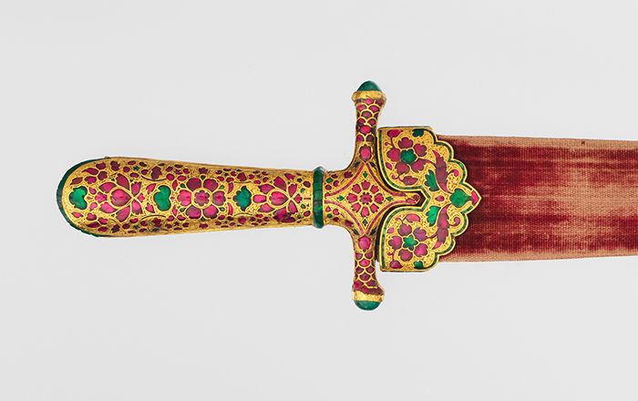 Close-up view of a gold dagger hilt, with inlaid rubies and emeralds, designed in floral forms and top of red sheath