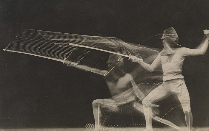 Black and white photograph of fencer lunging forward and standing back in a squat position