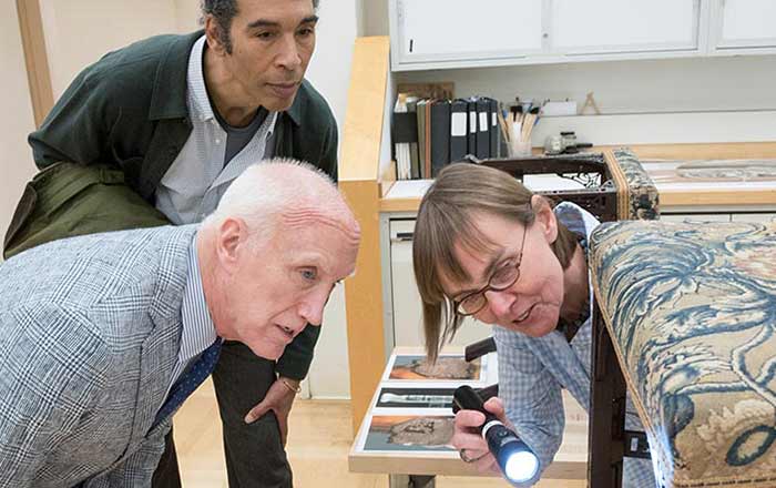 Conservator Mechthild Baumeister points a flashlight at a piece of furniture for a visitor to the conservation studio