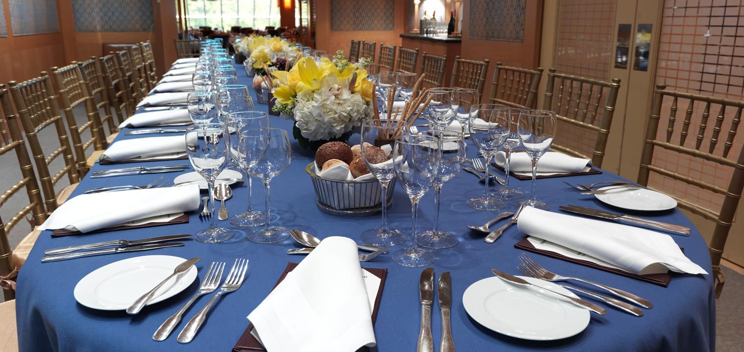 Long table set with a blue cloth, white plates and silverware