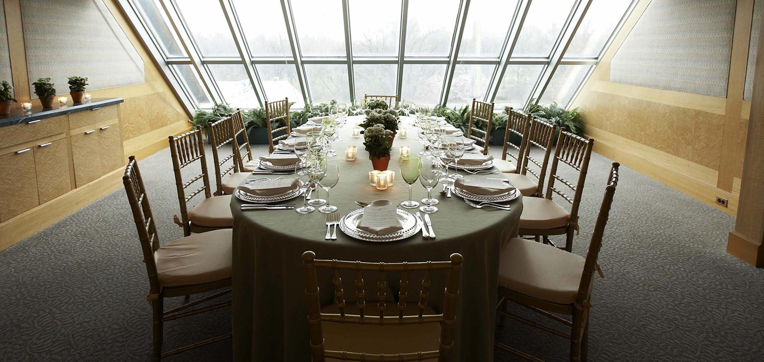 Long table with green cloth and white plate settings in front of a window 