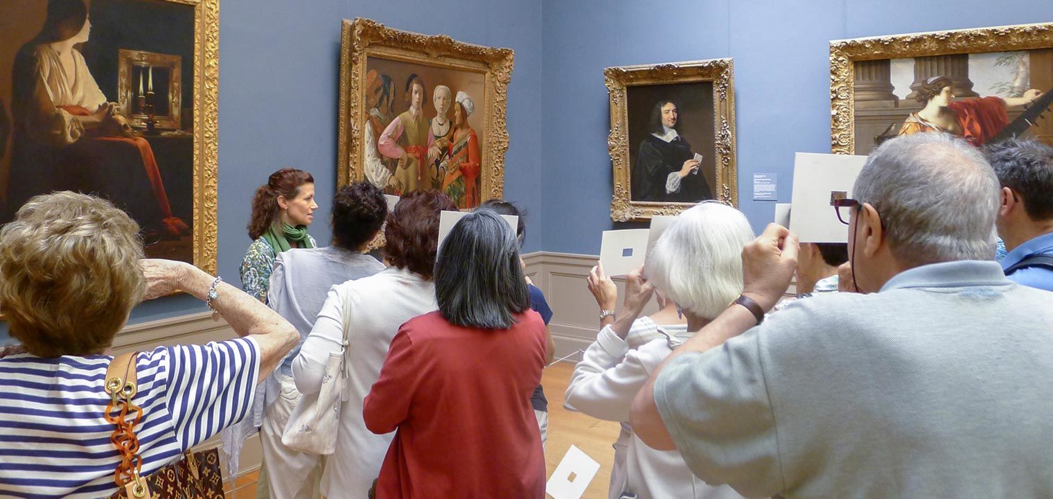 Adult programs gallery talk with visitors holding cardboard cutout to view paintings