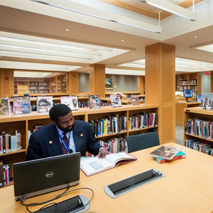 A modern, well-lit, spacious, and open library with low bookshelves filled with books and large tables for researchers