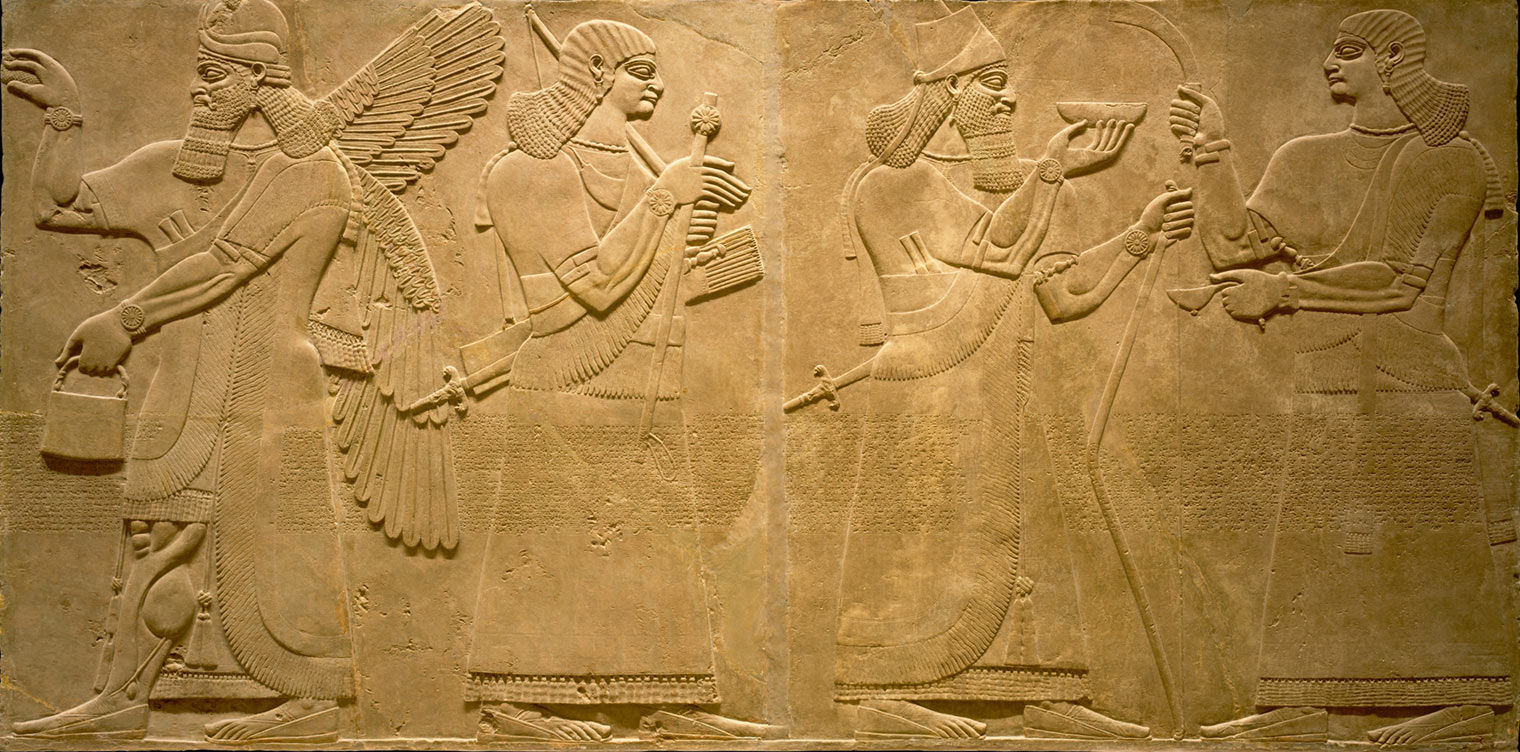 A close-up of a large stone relief panels depicting a long-haired bearded king in a conical cap with a small peak and a long diadem (the royal crown); he holds a bow, and a ceremonial bowl; facing him, is a beardless man carrying a fly whisk and a ladle