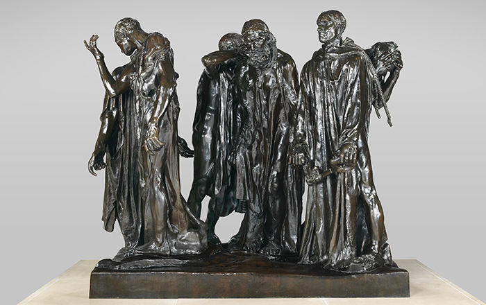 An over-life size bronze sculpture of a group of men chained together in a group, walking in a circle