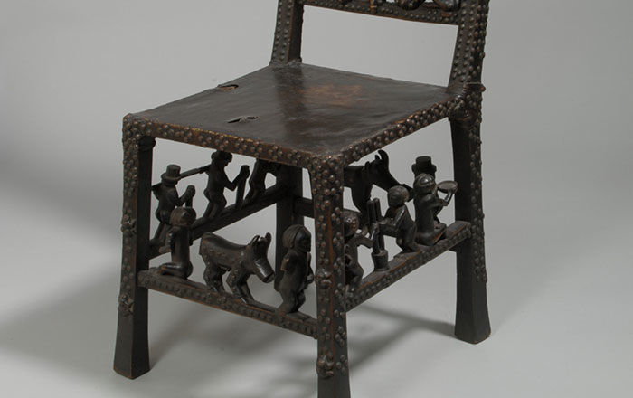 A dark wood African side chair decorated with seated figures and animals on the chair back, and on the rungs between the legs 