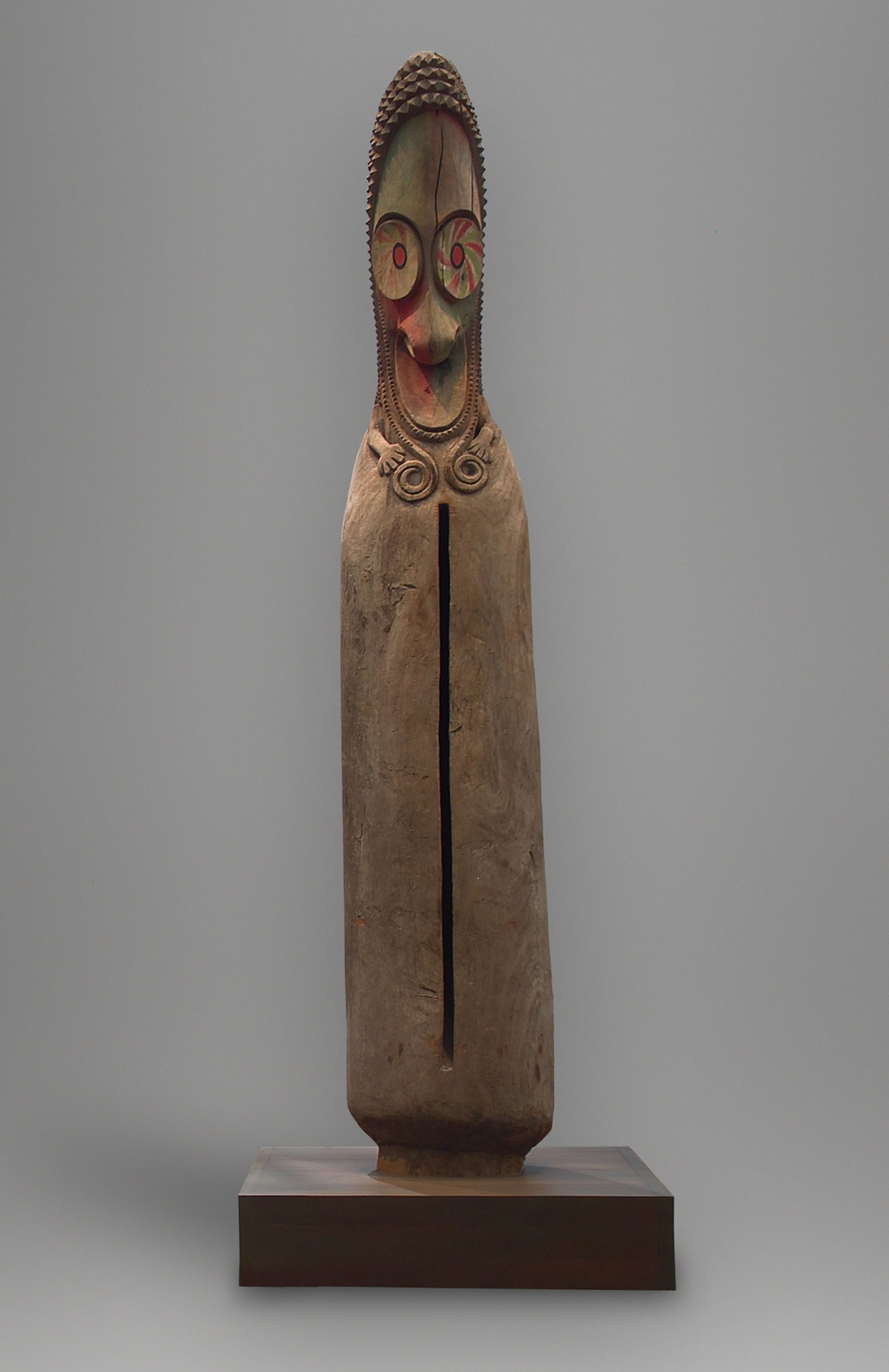 A hollow, wooden Oceanic sculpture with a bird-like face, large round eyes, sharp down-turned beak, and pointed head