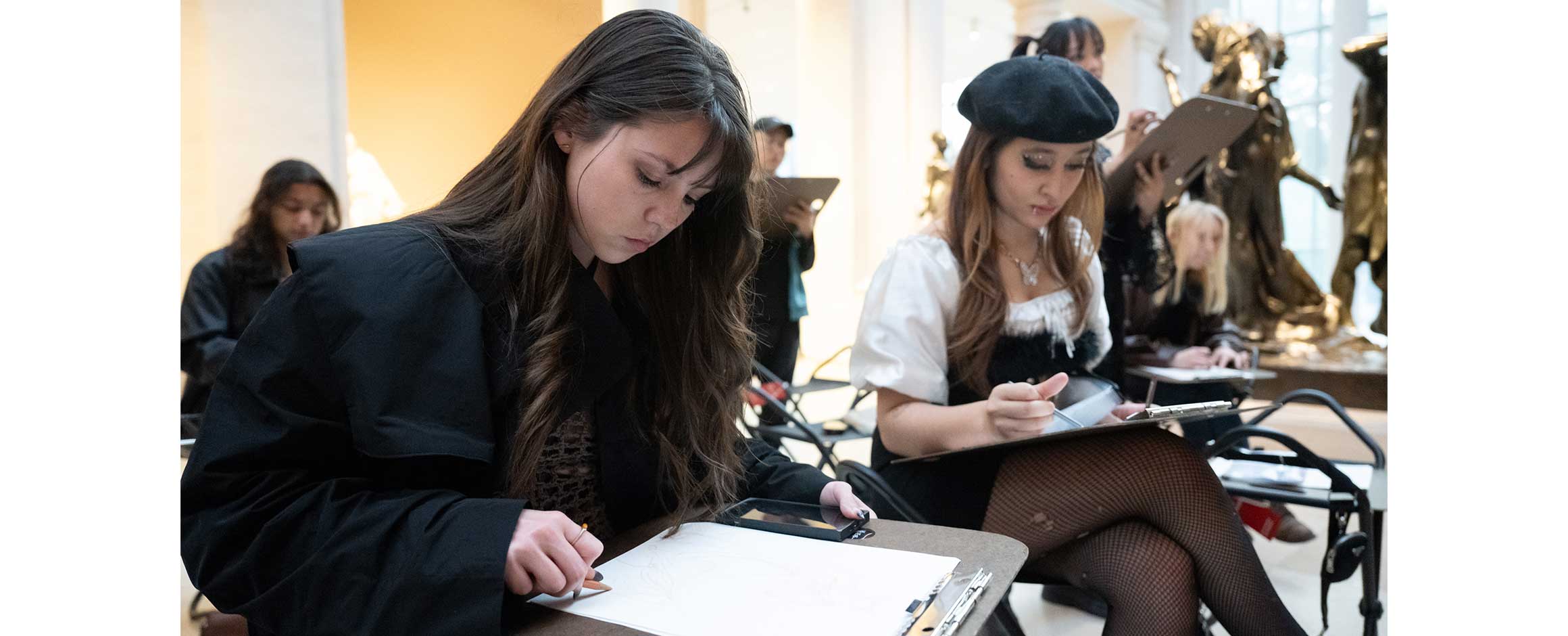 Two young women are sitting in a gallery and drawing.