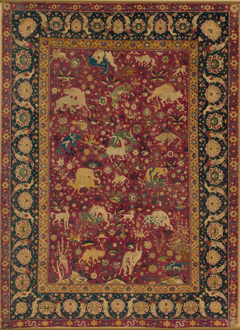 A red, woven silk carpet depicting images of animals in combat against a background of flowering plants. The range of animals includes lions, tigers, and rams, as well as spotted dragons and horned, deerlike beasts borrowed from Chinese art.