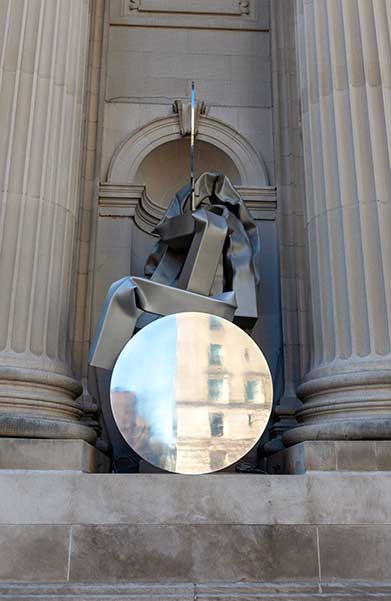 A stainless steel and aluminum sculpture with a reflective, circular disc and large, bending tubes